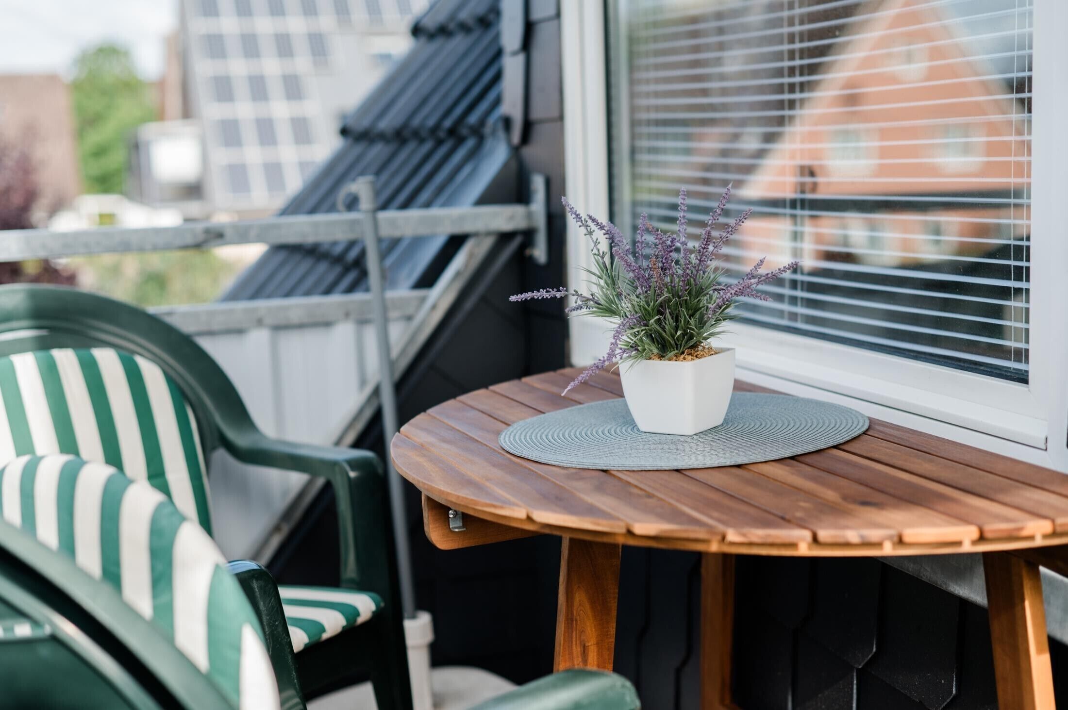 Una mesa de madera con una planta de lavanda en maceta, una silla verde a rayas y una ventana con persianas.