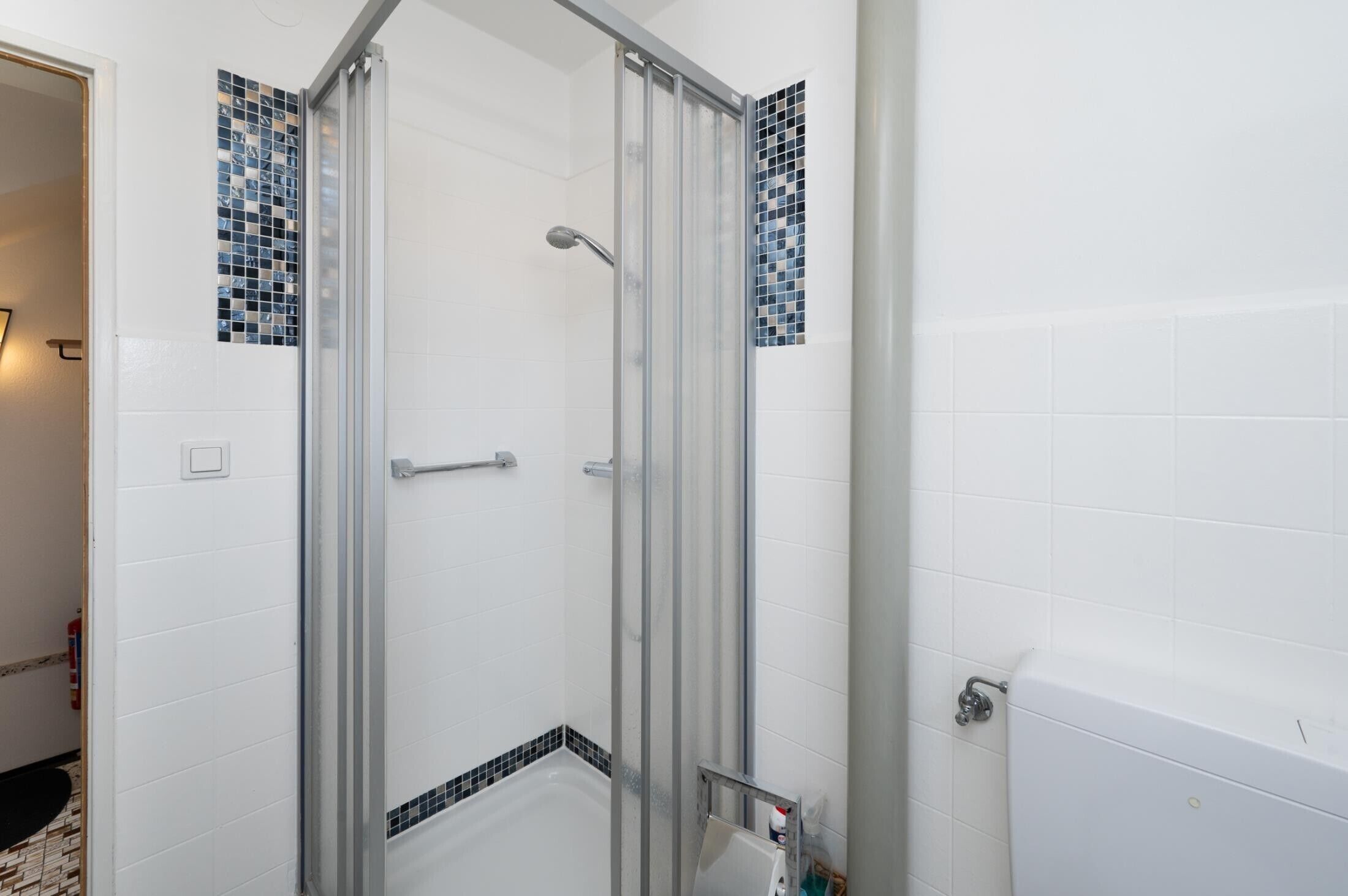 Een badkamer met een douchecabine van glas, witte betegelde wanden en een witte badkuip.