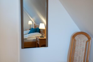 Ein Schlafzimmer mit einem Bett, Nachttischlampen, einem Beistelltisch und einem Spiegel, der den Raum wiederspiegelt.
