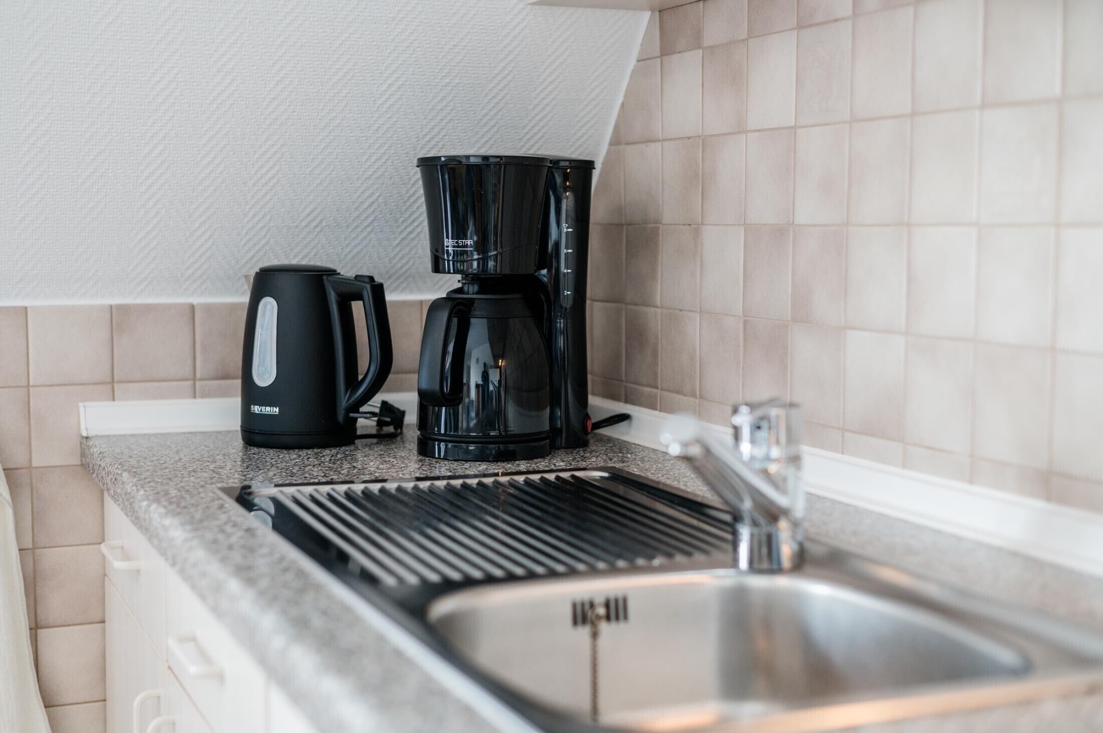 A kitchenette with a coffee maker, a kettle, and a sink.