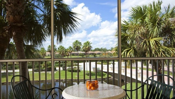 A balcony with a round table and chairs, overlooking a well-maintained lawn and palm trees.