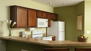 A kitchen with wooden cabinets, a white refrigerator, a microwave, and a stove. There is a vase with flowers on the counter. - Port St. Lucie | Golf Retreat | Pool + Spa | 2BR (Port St. Lucie)