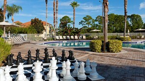A chessboard set up outdoors with palm trees and a pool in the background.