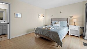 Une chambre à coucher comprenant un lit, des tables de chevet, une commode, un miroir et un luminaire fixé au mur.