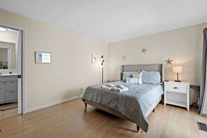 A bedroom with a bed, bedside tables, a nightstand, a mirror, and a wall-mounted light fixture. - Amazing Wildlife, Golf Cart Included - 15 Fairway Club (Fripp Island)