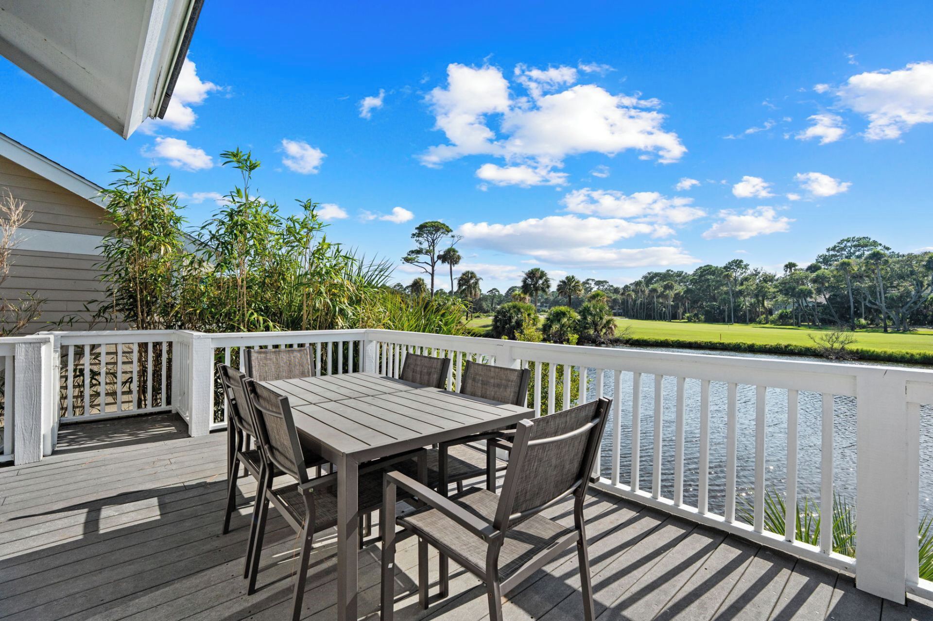 A wooden deck with a table and chairs, overlooking a golf course and water.