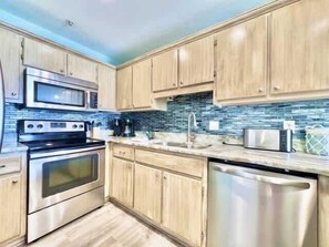 A modern kitchen with stainless steel appliances, wooden cabinets, and a blue-tiled backsplash. - Beachside Condo in Miramar Beach (Destin)