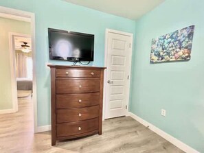 A room with a wooden dresser, a television mounted above it, and a door to the right. - Beachside Condo in Miramar Beach (Destin)