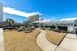 A courtyard with a pathway, a building with a flat roof, and a tall structure in the background. - Beachside Condo in Miramar Beach (Destin)