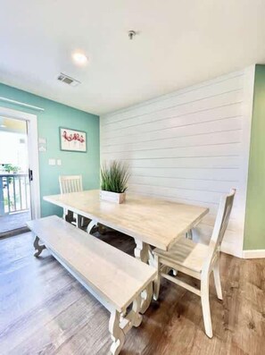 A dining area with a wooden table and benches, a potted plant, and a white wall with horizontal lines. - Beachside Condo in Miramar Beach (Destin)