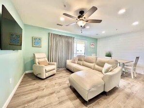 A living room with a sectional sofa, a recliner, a ceiling fan, and a dining area with a table and chairs. - Beachside Condo in Miramar Beach (Destin)