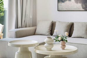 Un salon moderne avec un canapé, deux tables d’appoint et un vase rempli de fleurs.