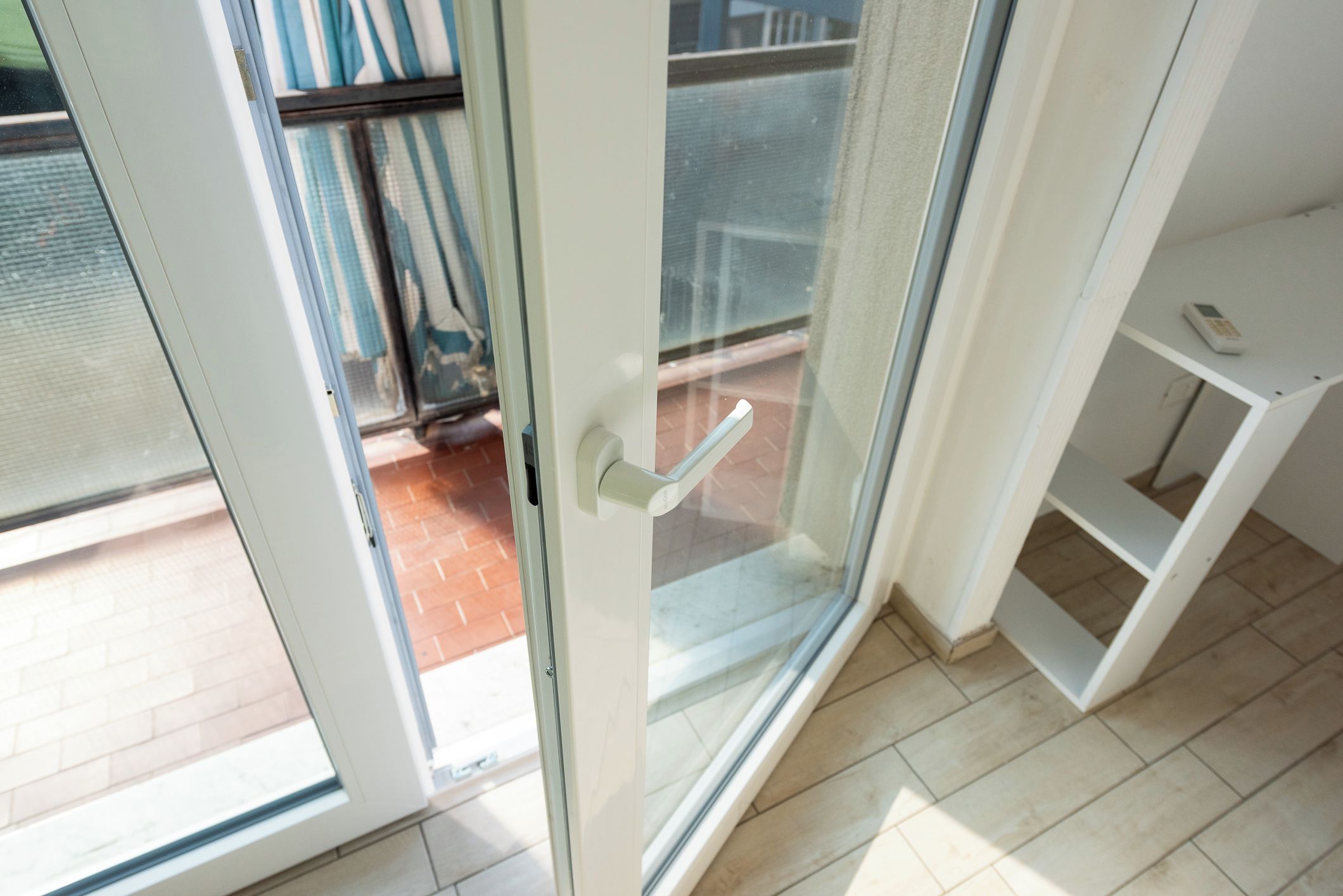 A room with a sliding glass door leading to an outdoor area with a metal gate and a tiled floor.