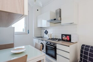 A compact kitchen with a gas stove, oven, washing machine, and a small dining area with a table and chairs. - Niguarda Suite (Milano)
