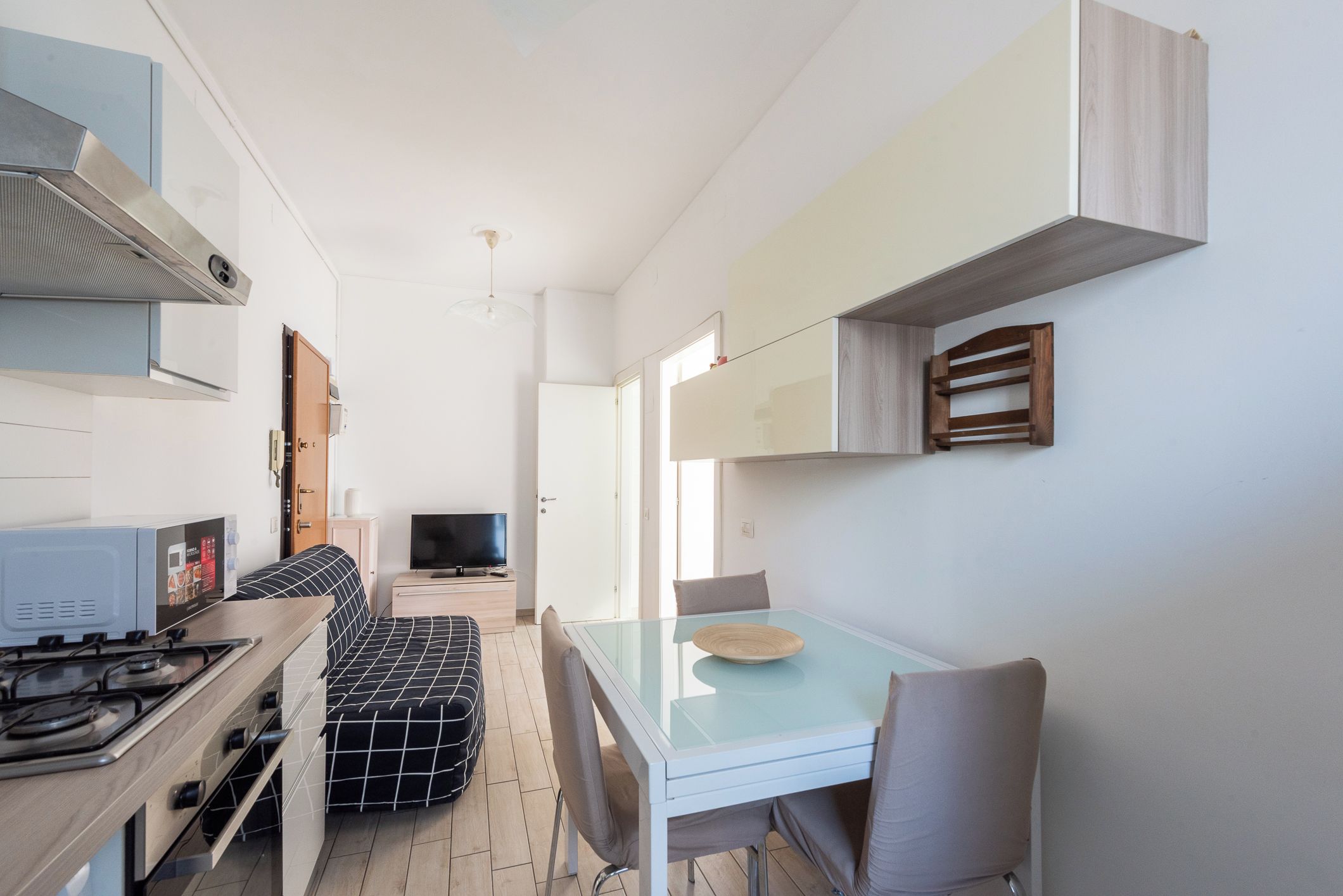 A compact kitchen with a gas stove, a sofa, and a dining table with chairs.