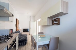 A compact kitchen with a gas stove, a sofa, and a dining table with chairs. - Niguarda Suite (Milano)