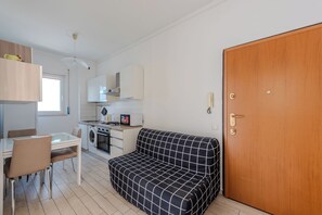 A compact kitchen with a dining area, a sofa, and a wooden door. - Niguarda Suite (Milano)