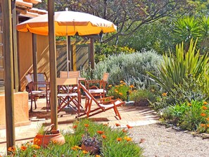 Ein Sitzbereich im Freien mit Holzkästen und einem Tisch, umgeben von einem Garten mit verschiedenen Pflanzen und Blumen.