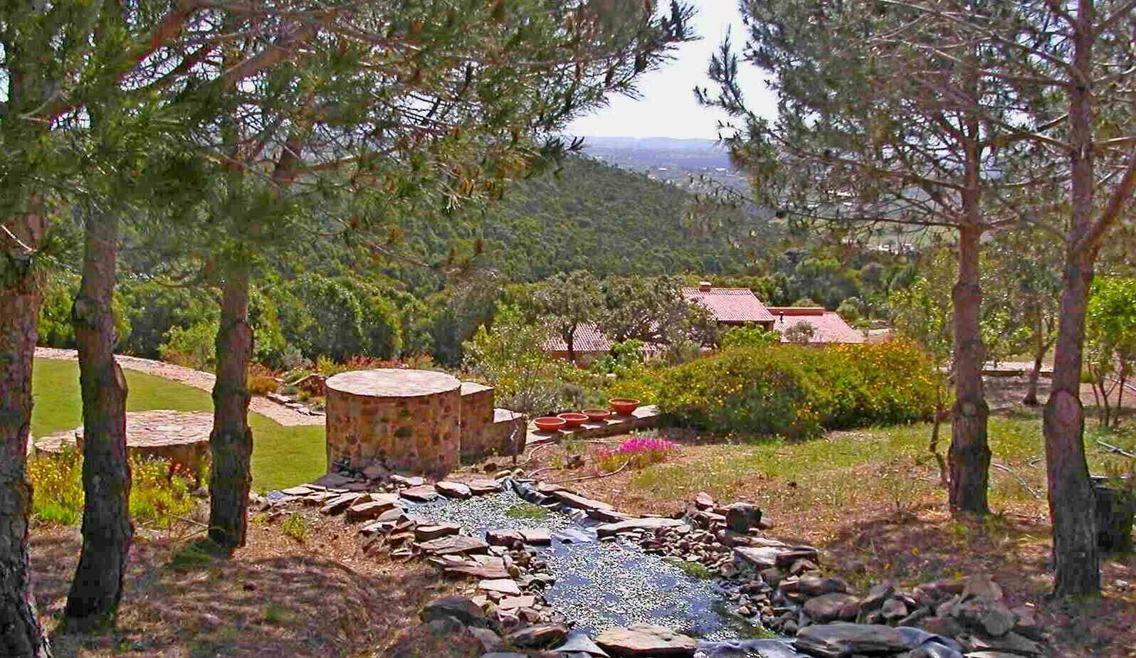 A garden with a stone fountain, trees, and a view of a distant town.