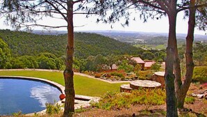 Piscina rodeada por um jardim ajardinado com árvores e vista para uma paisagem distante.