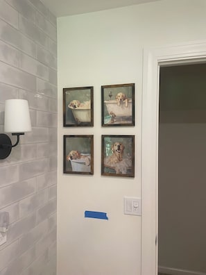 A bathroom with four framed dog paintings on the wall, a wall-mounted light fixture, and a door.