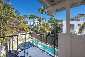 A balcony with a pool, surrounded by palm trees and modern buildings.