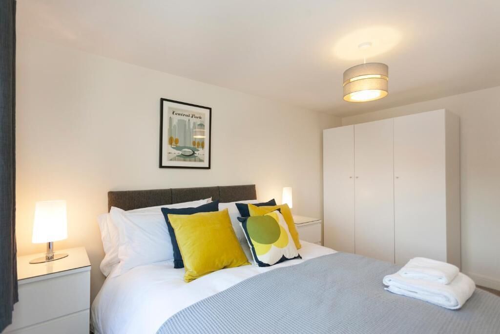 Ein Hotelzimmer mit einem Bett, einem Nachttisch, einer Lampe, einem gerahmten Bild an der Wand und einem Kleiderschrank.