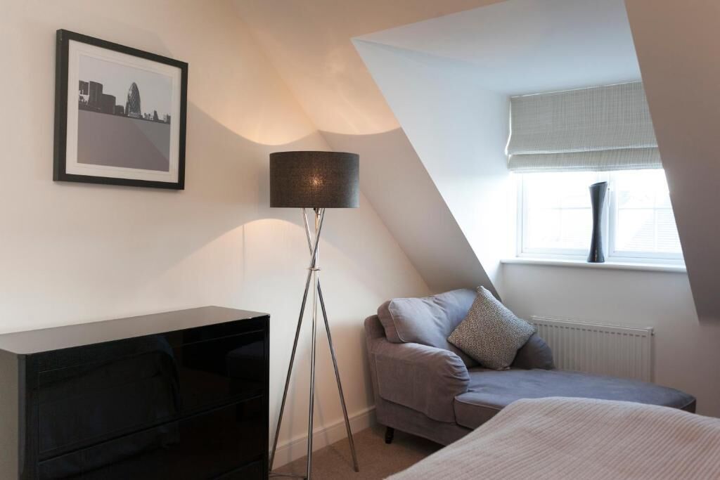 Ein Schlafzimmer mit einem Bett, einem Sofa, einer Stehlampe, einem gerahmten Bild an der Wand und einem Fenster mit Heizkörper.