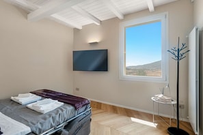 Une chambre à coucher avec un lit, un téléviseur à écran plat fixé au mur, une fenêtre donnant sur un paysage agréable et une petite table sur laquelle sont posés quelques objets.
