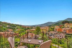 A balcony with a table and chairs, overlooking a hillside village with buildings and greenery. - [Residenza la Guercia]Seaview-5 terre-A/C (La Spezia)