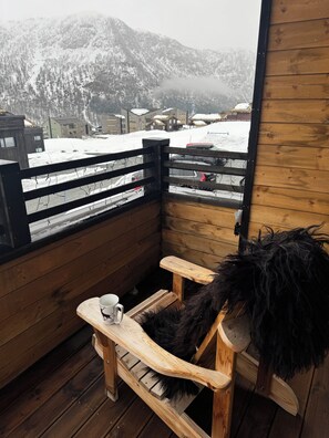 Une terrasse en bois avec un banc et une tasse, donnant sur un paysage montagneux enneigé.