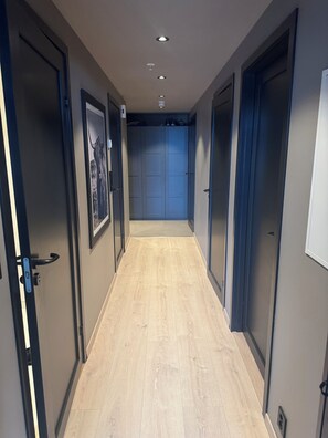 Un couloir doté d’un plancher en bois, de luminaires encastrés au plafond et de portes fermées de part et d’autre.
