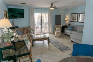 A living room with a sofa, coffee table, and a TV. There is a balcony with a view of the outside. - Beachfront Villa with Sea Views  Bikes Included  Gulf Across St   Kayak Access (Miramar Beach)