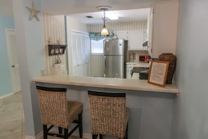 A kitchen with a stainless steel refrigerator, a microwave, and a small island with two wicker chairs. - Beachfront Villa with Sea Views  Bikes Included  Gulf Across St   Kayak Access (Miramar Beach)