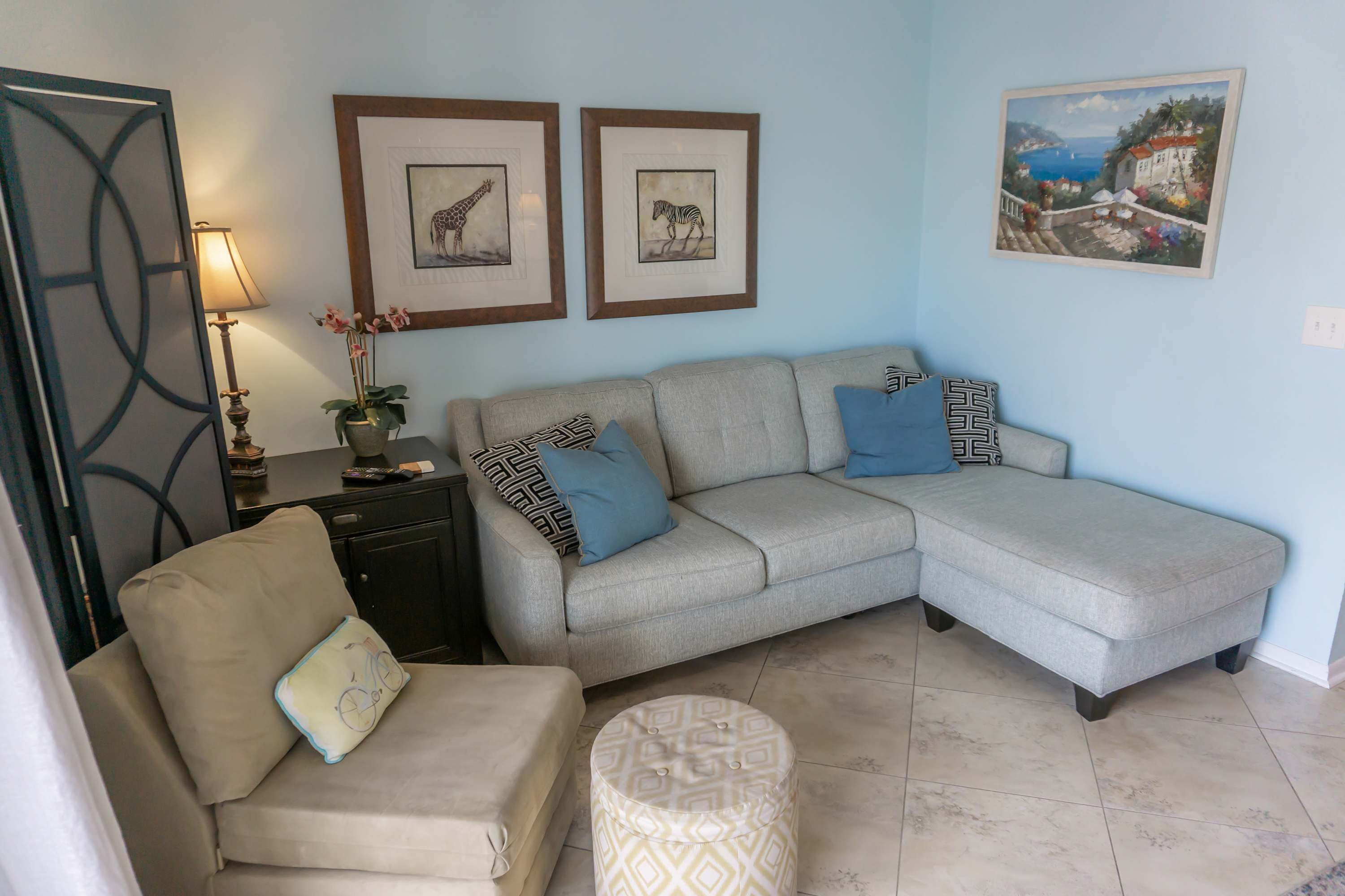 A living room with a sofa, a chair, and a small ottoman. There are framed pictures on the wall.