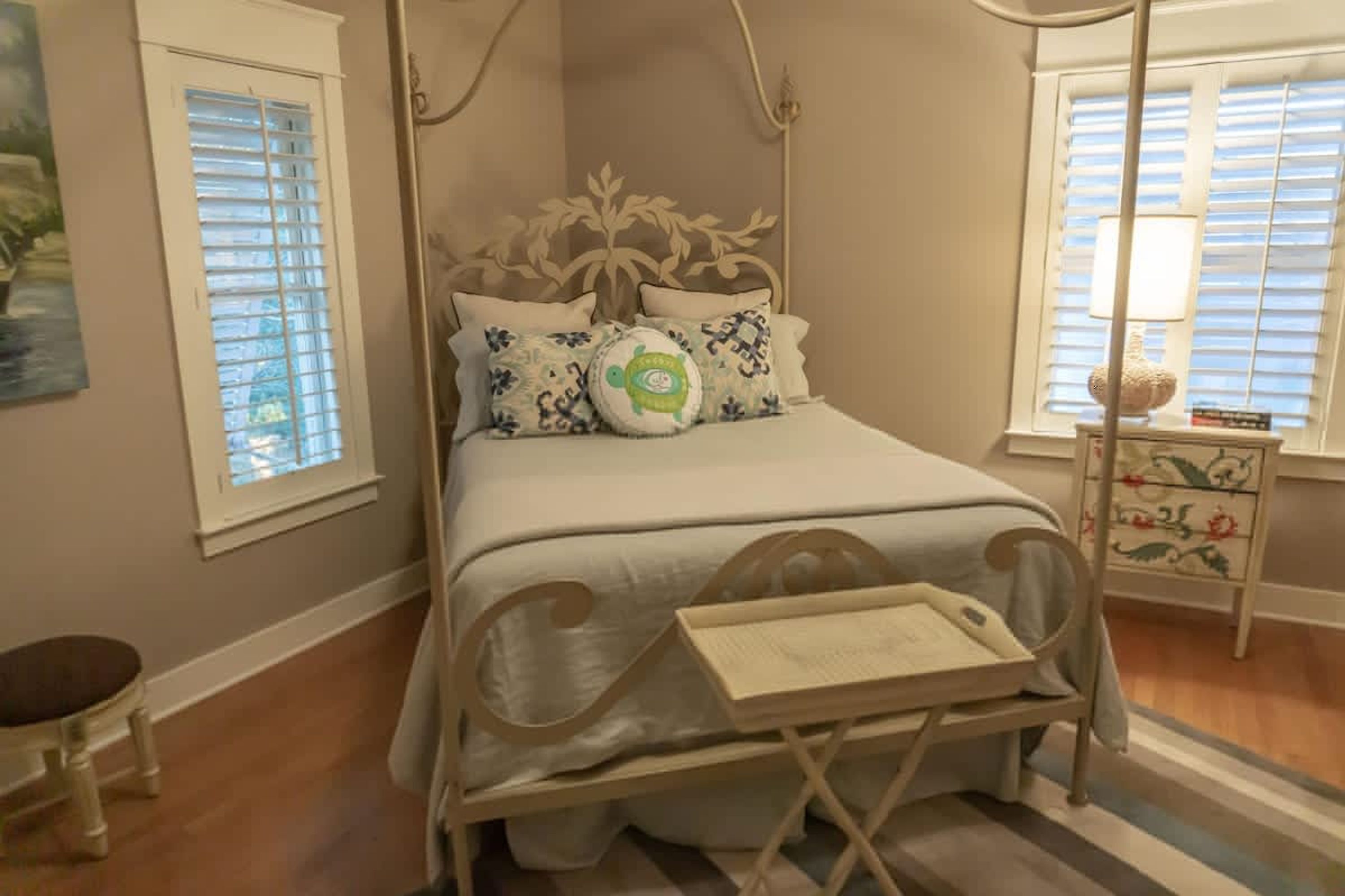 A bedroom with a canopy bed, a bedside table with a lamp, and a dresser with floral patterns.