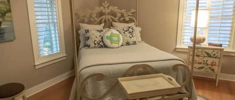 A bedroom with a canopy bed, a bedside table with a lamp, and a dresser with floral patterns.