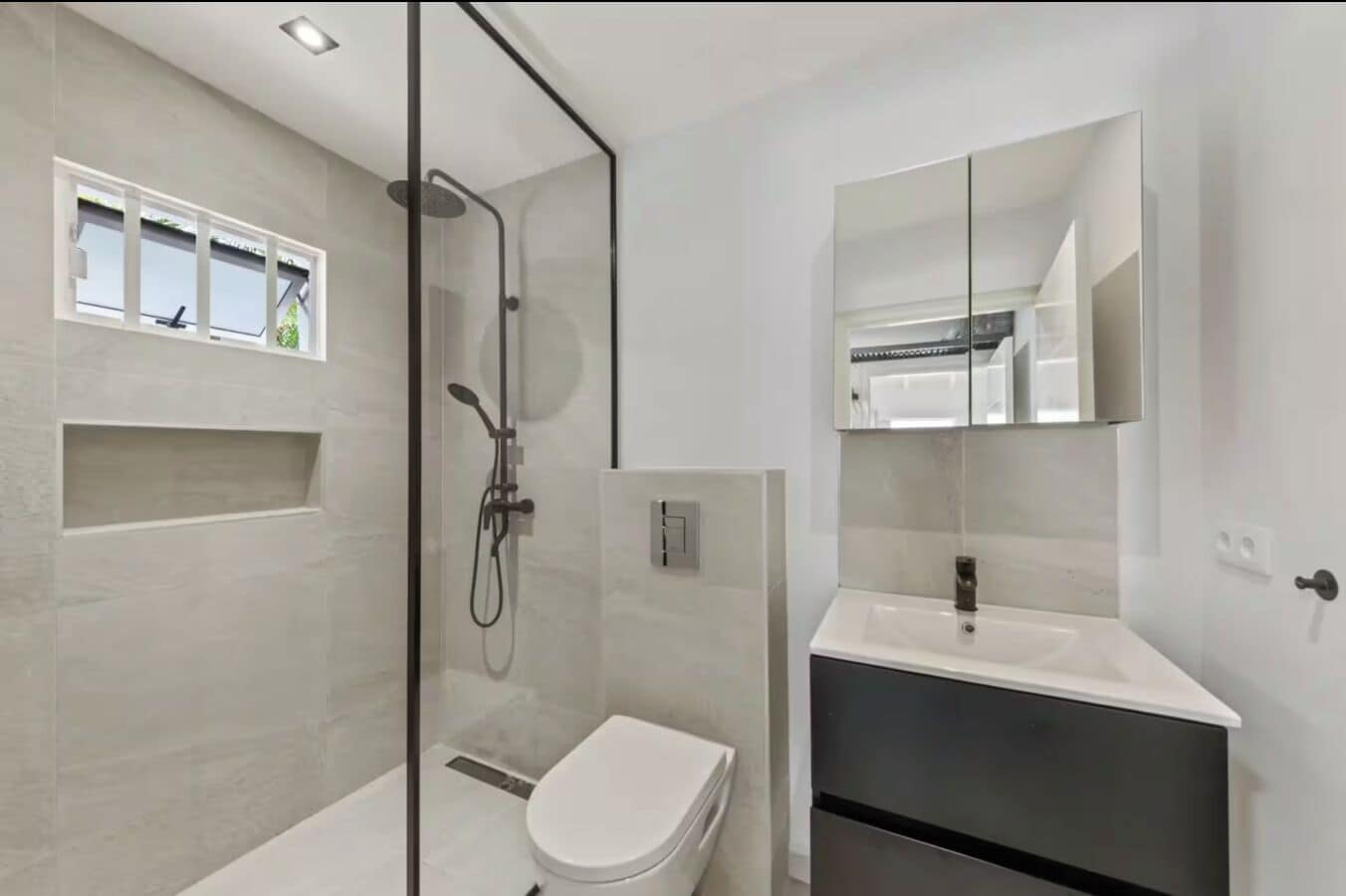 A modern bathroom with a glass-enclosed shower, a white toilet, and a vanity with a mirror.