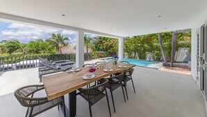 Un espacio de comedor al aire libre con piscina, rodeado de vegetación y un cielo despejado.