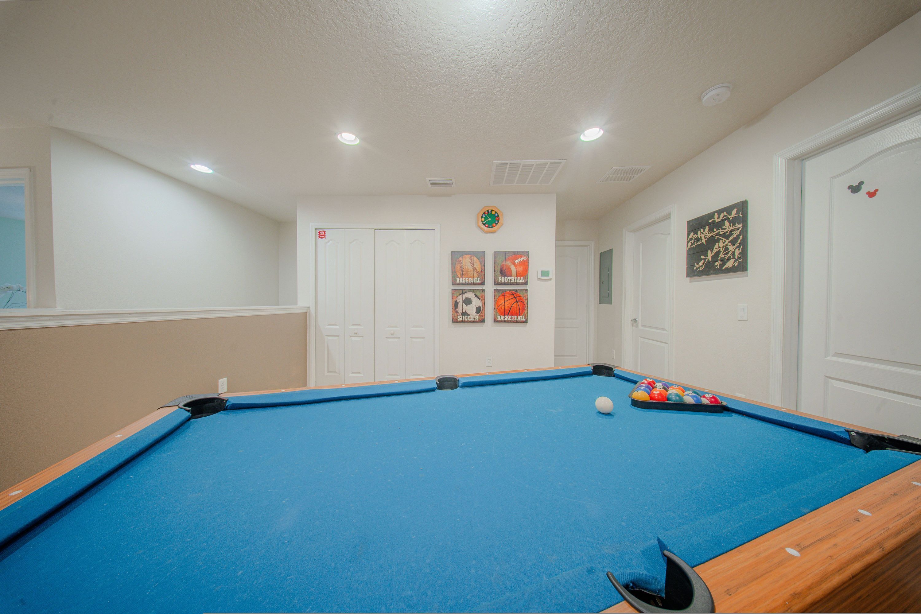 Une table de billard avec une boule blanche, entourée de murs décorés sur le thème du sport et surmontée d’une horloge.