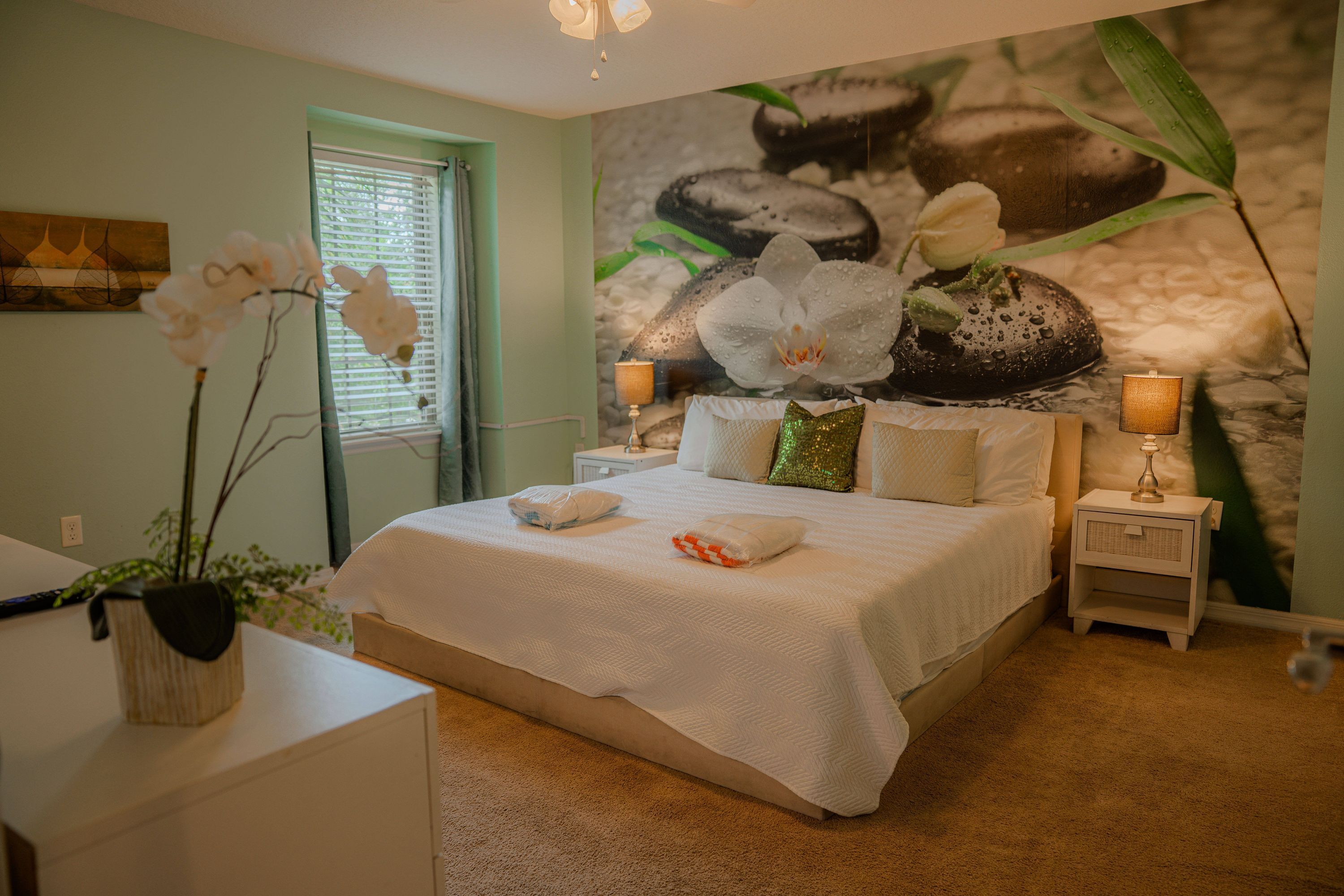 Een slaapkamer met een bed, twee nachtkastjes, een wandpaneel en een raam met jaloezieën.