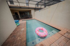 Ein Swimmingpool mit einem rosa Schwimmreifen, umgeben von einer Pflasterterrasse.