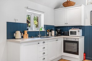 Une cuisine moderne avec des meubles blancs, un four à micro-ondes, une bouilloire et une fenêtre donnant sur un paysage verdoyant.