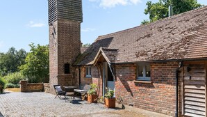 A brick building with a chimney, a small porch with a bench, and a cobblestone patio. - Tea Hut By My Getaways (Uckfield)