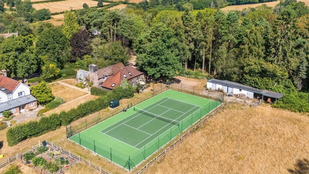 An aerial view of a residential area with a tennis court, houses, and surrounding greenery. - Tea Hut By My Getaways (Uckfield)