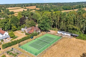 Una cancha de tenis rodeada de edificios residenciales y un paisaje boscoso.