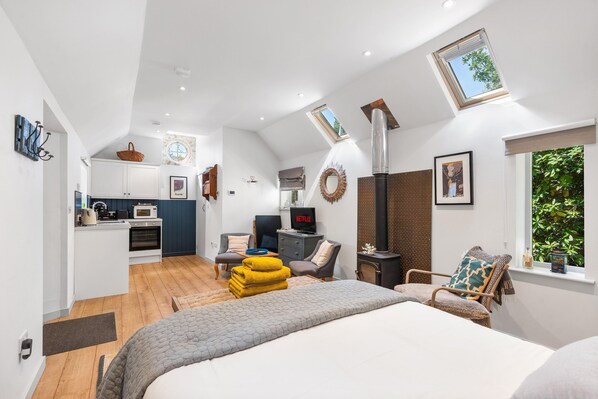 A modern interior with a kitchen, dining area, and a bedroom with a large bed and a fireplace. - Tea Hut By My Getaways (Uckfield)