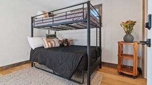 A bunk bed with a black metal frame, a grey mattress, and a wooden side table with a vase of flowers.