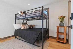 A bunk bed with a black metal frame, a grey mattress, and a wooden side table with a vase of flowers.