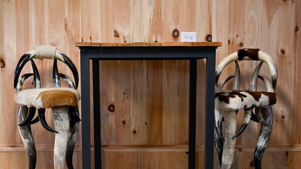 Two chairs with antler backs and a table in front of a wooden wall.
